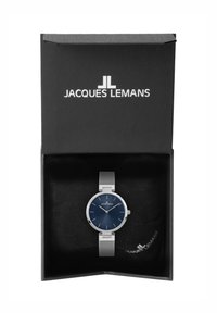 Reloj con correa de malla plateada y esfera redonda de color azul marino, con marcas horarias plateadas y logotipo. Presentado en una caja negra con un suave forro interior.