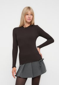 Maglietta marrone a maniche lunghe con una texture a coste e scollatura ondulata. Abbinata a una gonna grigia a pieghe legata in vita.