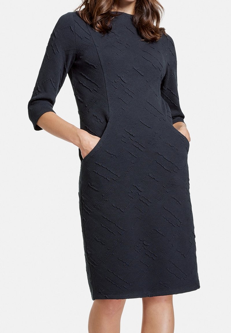 Abito blu navy con maniche a tre quarti, tessuto testurizzato, tasche laterali e una silhouette aderente fino al ginocchio.