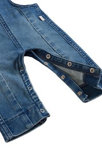 Denim mouw met drukknoopjes langs de naad, gedeeltelijk losgeknoopt, met zichtbare blauwe stof en stikdetails op een witte achtergrond.