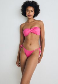 Bikini set in vibrant pink. bandeau top with twisted design, adjustable tie-side bottoms. Smooth texture, minimal hardware details.