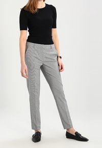 Grå mønstrede bukser med en skræddersyet pasform, der har et subtilt houndstooth-mønster, sidelommer og en glat overflade. Sættes sammen med en sort ribbet top.