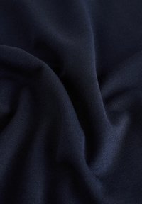 Merenno sininen kangas, jossa on sileä pinta, taitettu niin, että näkyvät pehmeät, laskeutuvat ominaisuudet. Materiaali on kevyt ja siinä on hienovarainen kiilto.