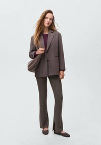 Blazer à carreaux marron sur un pull en maille bourgogne, associé à un pantalon marron côtelé avec fentes latérales et des ballerines à clous marron foncé.