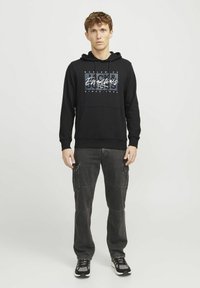 Black hooded sweatshirt with graphic design on front, paired with dark cargo pants featuring multiple pockets and a loose fit, worn with black sneakers.