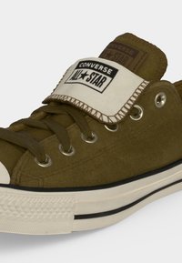 Πράσινο παπούτσι Converse All Star που δείχνει κορδόνια, μεταλλικά κορδονότρυπα και διπλωμένη γλώσσα με ορατό λογότυπο και λεπτομέρειες από καουτσούκ στην σόλα.