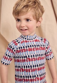 Kurzärmeliges Rashguard mit hellblauem Grundton und einem wiederholenden Muster von uniformierten Wachen in Rot und Blau. Glattes Gewebe, figurbetontes Design.