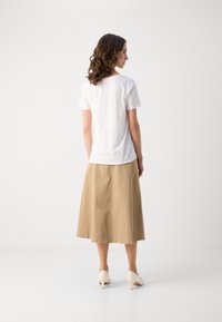 Hvit kortermet t-skjorte kombinert med en beige midiskjørt og lyse hæler, med et enkelt design og myk tekstur.