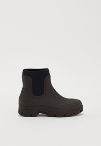 Botas de goma negras hasta el tobillo con suela gruesa y antideslizante y paneles laterales elásticos para ponerse fácilmente, diseñadas para su uso en clima húmedo.