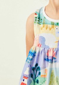 Dítě oblečené v bezramínkových šatech s barevnými ilustracemi zvířat, stromů, majáku a vody na světlém pozadí.