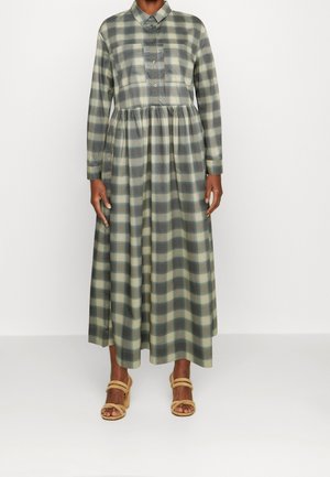 Lungo vestito a scacchi in tonalità di verde e beige, con bottoni frontali, colletto e vita arricciata. Indossato con sandali beige con zeppa.