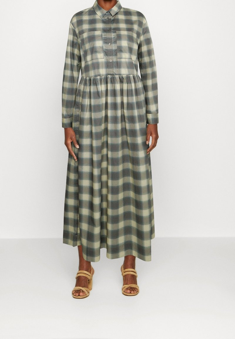 Lång rutig klänning i nyanser av grön och beige, med knäppning framtill, krage och samlad midja. Bärs med beige plattformssandaler.
