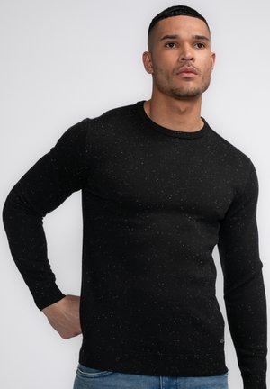 Schwarzer Strickpullover mit Rundhalsausschnitt, der ein strukturiertes Muster aus kleinen weißen Punkten aufweist. Rippbündchen an den Ärmeln und am Saum sorgen für zusätzliche Details.