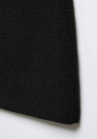 Gros plan sur un tissu noir avec un motif tissé texturé et des fibres visibles sur un fond blanc.