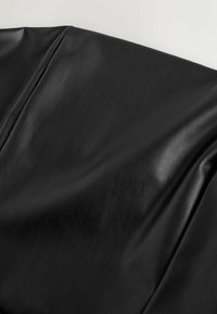 Musta tekonahkakangas, jossa on sileä rakenne ja hienovarainen kiilto, pehmeillä poimuilla ja lievällä puukuvioinnilla.