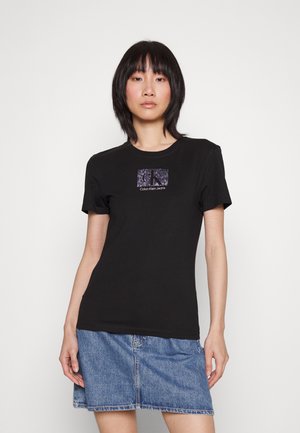 Camiseta de algodón negra con mangas cortas, que presenta un diseño de logo rectangular en púrpura y blanco. Forma ajustada, textura suave.