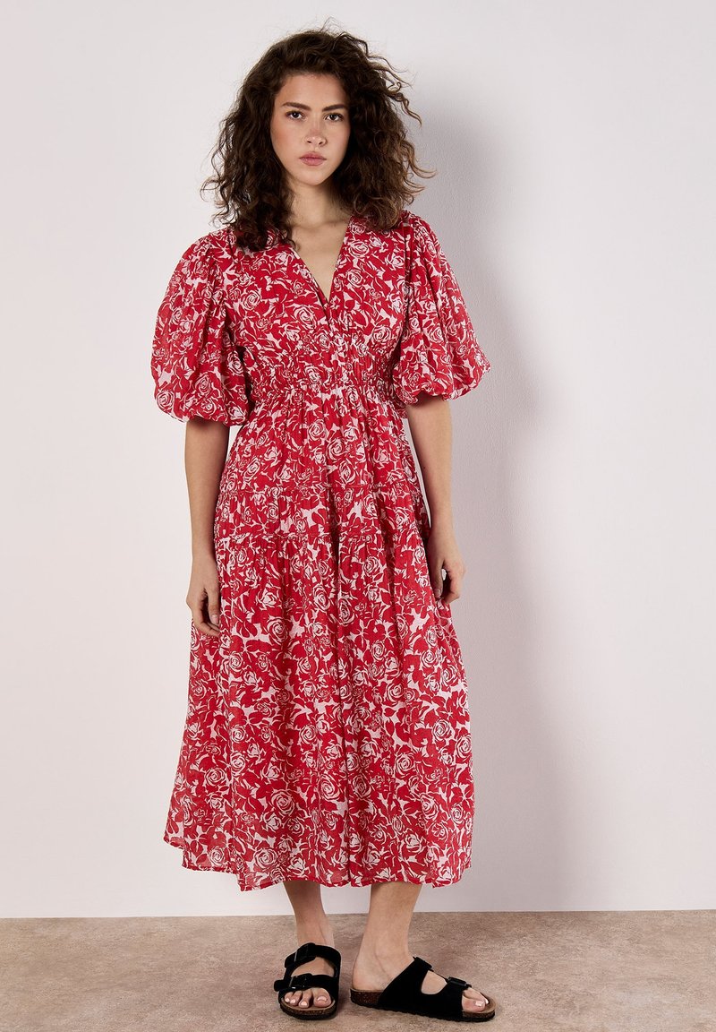Rotes Blumenkleid mit Puffärmeln und V-Ausschnitt. Hergestellt aus leichtem Stoff, hat einen elastischen Bund und einen fließenden, knöchellangen Rock.