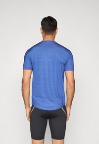 Μπλε αθλητική μπλούζα με υφασμάτινο μοτίβο, κοντά μανίκια και στρογγυλεμένη τελείωμα, φορεμένη πάνω από εφαρμοστά μαύρα σορτς.