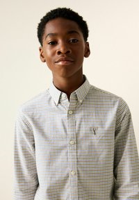 Kockás, gombos ing világoskék és barna árnyalatokban. Gallérral és a mellrészen kis logóval rendelkezik. Simogató pamut anyagból készült.