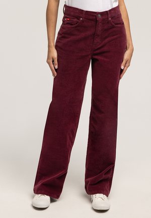 Bordowe spodnie sztruksowe o szerokich nogawkach z fakturowanej tkaniny, z pięcioma kieszeniami i zapięciem na guziki, w połączeniu z białymi trampkami.