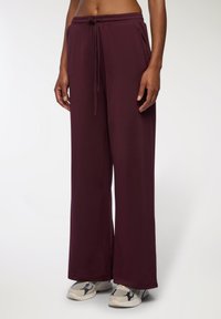 Pantaloni da jogging a gamba larga bordeaux con cintura elastica e cordoncino. Tessuto morbido, tasche laterali e vestibilità comoda.