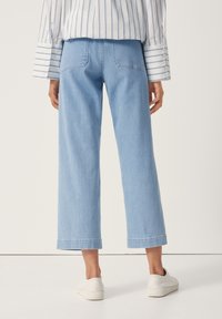 Světlé modré džíny s širokými nohavicemi a přímým střihem, vybavené zadními kapsami a čistým lemem. Kombinované s bílými nazouvacími botami.