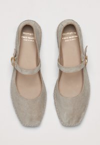 Zapatos Mary Jane de ante beige con punta cuadrada, tacón plano y una correa con un hebilla de tono dorado. Costuras beige acentúan la suela.