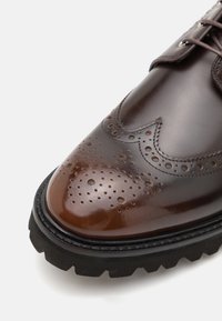 Hnědá kožená bota s leštěnou špičkou s perforovanými detaily, brogue akcenty a silnou černou gumovou podrážkou.