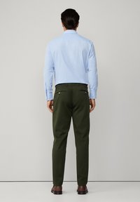 Cămașă bleu deschis cu nasturi și pantaloni verzi, ambele cu un design ajustat. Pantalonii au buzunare la spate cu nasturi. Pantofii maroon completează ținuta.