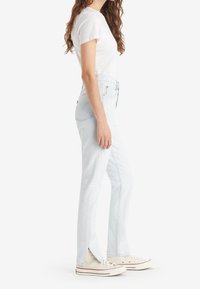 Vaqueros de tiro alto en azul claro con aberturas laterales, hechos de mezclilla. Combinados con una camiseta blanca ajustada y zapatillas bajas beige.