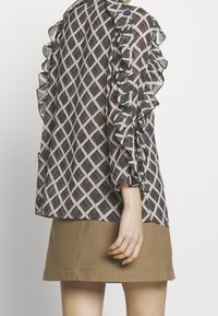 Schwarz-weiße gemusterte Bluse mit Rüschensäumen, kombiniert mit einem beigen Rock. Die Bluse weist ein geometrisches Diamantmuster auf.