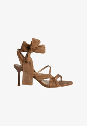 Sandalia de tacón alto marrón con un acento de lazo de tela texturizada, tiras entrelazadas y un tacón delgado y afilado. Planta suave con punta abierta.