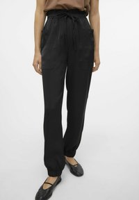 Zwarte lichtgewicht broek met een elastische tailleband met koord, zijzakken en elastische manchetten, gecombineerd met platte zwarte schoenen.