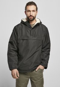Svart huva tröja med fleece-fodrad krage, framficka och elastiska �ärmslut. Bärs över en mörkgrön skjorta, kombinerad med cargobyxor.