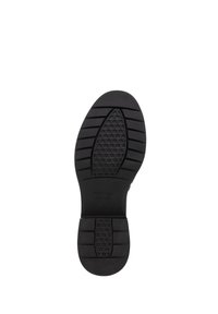 Czarna gumowa podeszwa buta o wzorze w kompozyty, teksturowane rowki i gładki obcas. Zawiera wytłoczone logo marki w pobliżu środka.