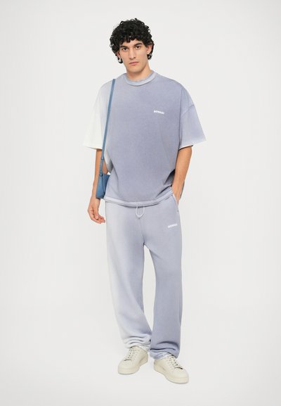 Μωβ βαθύ gradient φανελάκι oversized και φόρμες με άσπρο λογότυπο. Καθημερινό, μαλακό ύφασμα; αθλητικά παπούτσια με υφή. Επίσης περιλαμβάνεται τσάντα χιαστί.