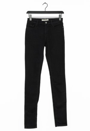 Black slim-fit jeans with front pockets and belt loops hanging on a black hanger against a white background.
