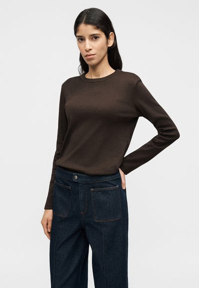 Καφέ μακρυμάνικο πουκάμισο με στρογγυλή λαιμόκοψη, συνδυασμένο με σκούρο μπλε τζιν παντελόνι που έχει δύο μπροστινές τσέπες και εμφανείς ραφές.