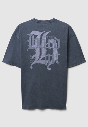 Maglietta in cotone grigio scuro con vestibilità over, caratterizzata da grandi grafiche testuali bianche sul retro, tra cui "New York City" e lettering stilizzato.