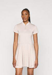 Kurzärmliges, hellbeiges Kleid mit einem Reißverschlusskragen und ausgestelltem Rock. Hergestellt aus glattem Stoff mit einem Logodetail auf der Brust.