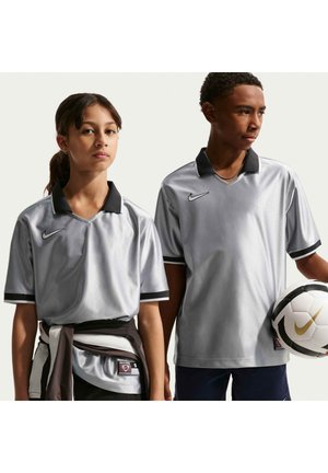 Twee jonge mensen dragen zilveren Nike voetbalshirts, één houdt een witte en gouden Nike voetbal vast.