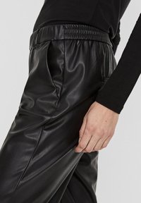 Black faux leather pants featuring an elastic waistband and smooth texture, with side pockets and a loose fit, showcasing subtle creases.