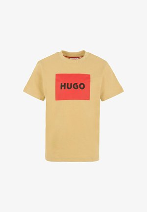 T-shirt beige a maniche corte con un logo rettangolare rosso sul davanti che mostra la parola "HUGO" in lettere nere in grassetto.