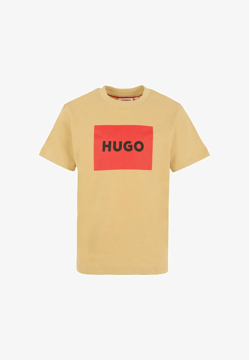 T-shirt beige à manches courtes avec un logo rectangulaire rouge affichant le mot "HUGO" en lettres noires en gras à l'avant.