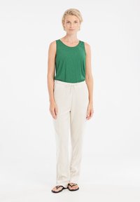 Canotta verde a righe, pantaloni bianchi leggeri con vita a cordino e infradito neri, indossati da un modello in piedi contro uno sfondo chiaro.