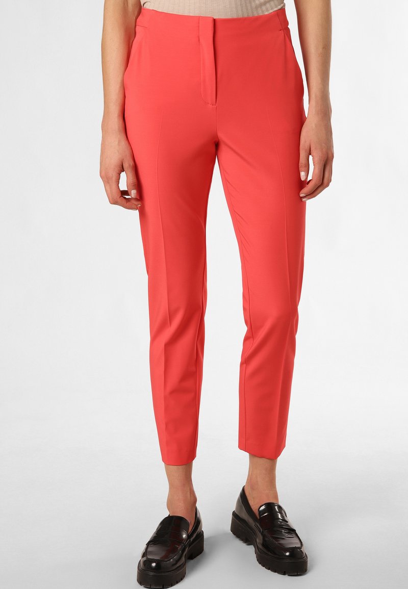 Pantalons taillés corail en tissu léger avec un front plat, des jambes fuselées et des poches latérales. Portés avec des mocassins noirs.