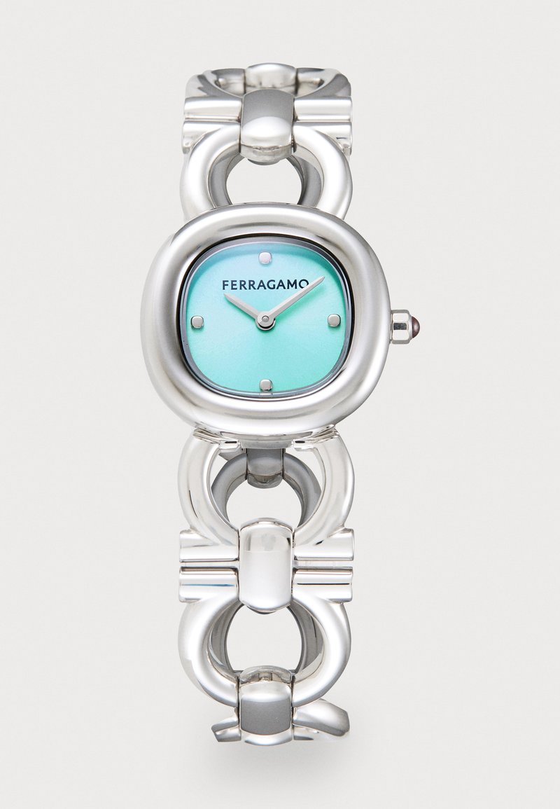 Reloj pulsera de metal plateado con una cara ovalada, esfera turquesa y manecillas plateadas. Diseño notable de eslabones entrelazados conecta los segmentos.