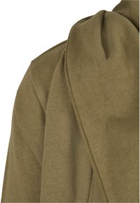 Olivgrüner Strickstoff mit einer weichen Textur. Verfügt über ein drapiertes Design und eine gefaltete Detail auf einer Seite. Flache Nähte sind entlang der Kanten sichtbar.