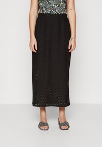 Svart midiskjørt i åpen mesh-design med fleksibel midje. Båret med grå slip-on sandaler med spenne-detalj.