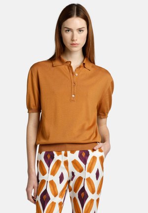 Kurze Ärmel Poloshirt in Camel, strukturiertes Strickmaterial mit Knopfleiste. Getragen mit gemusterten Hosen, die orangefarbene und lila Blattdesigns zeigen.